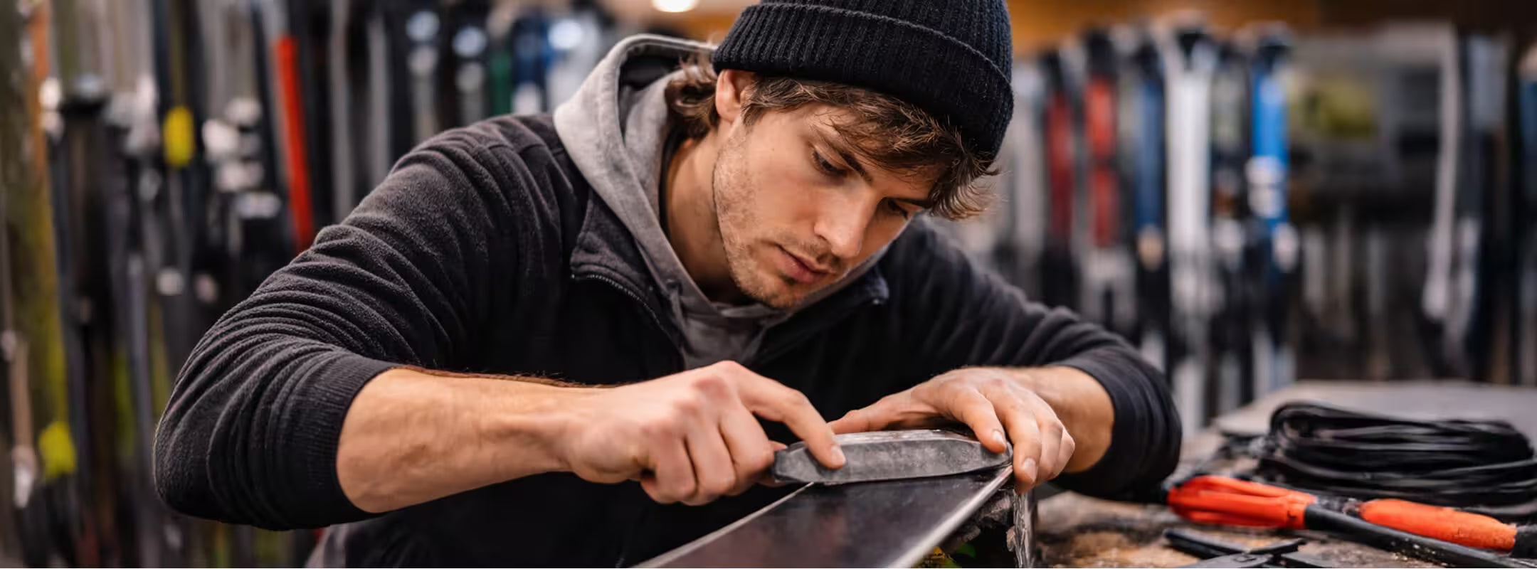 Man working on a ski in a workshop setting with tools and equipment around.