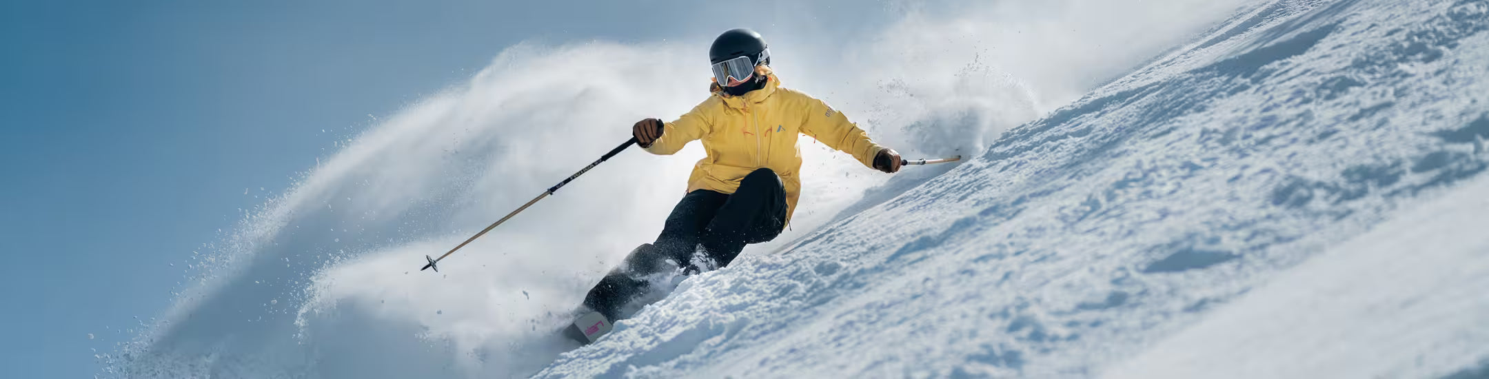 Person skiing down a snowy slope with a blue sky background