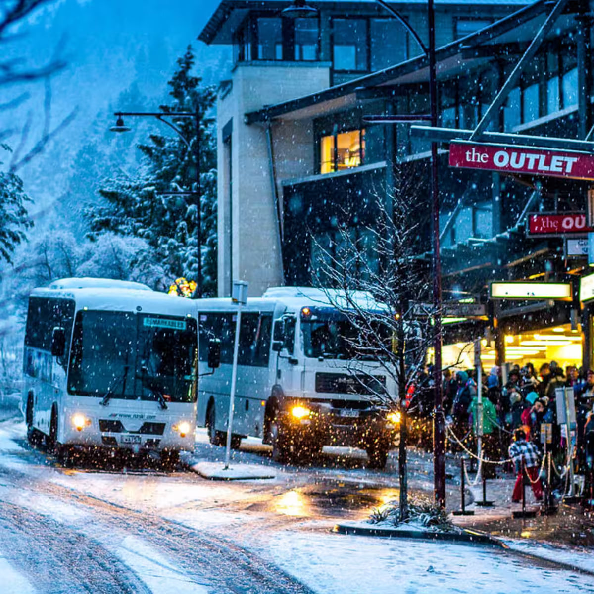 Buses in a snowy street with people gathered outside an outlet store.