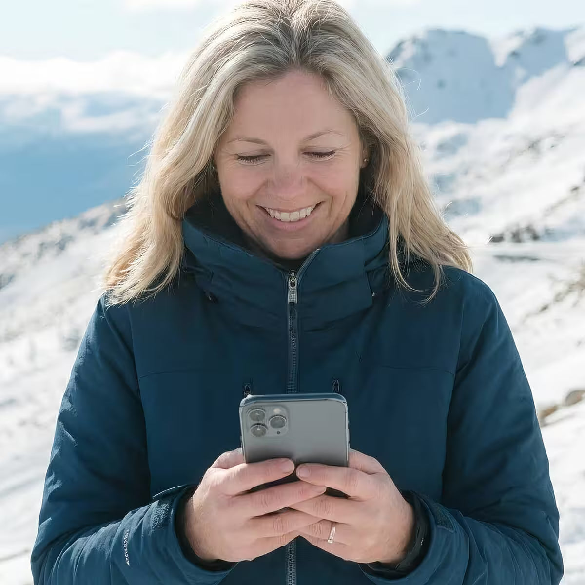 Woman in a blue jacket using a phone with snowy mountains in the background