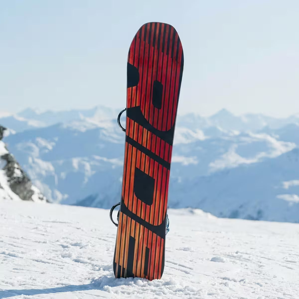 Red and black snowboard leaning against a snowy mountain