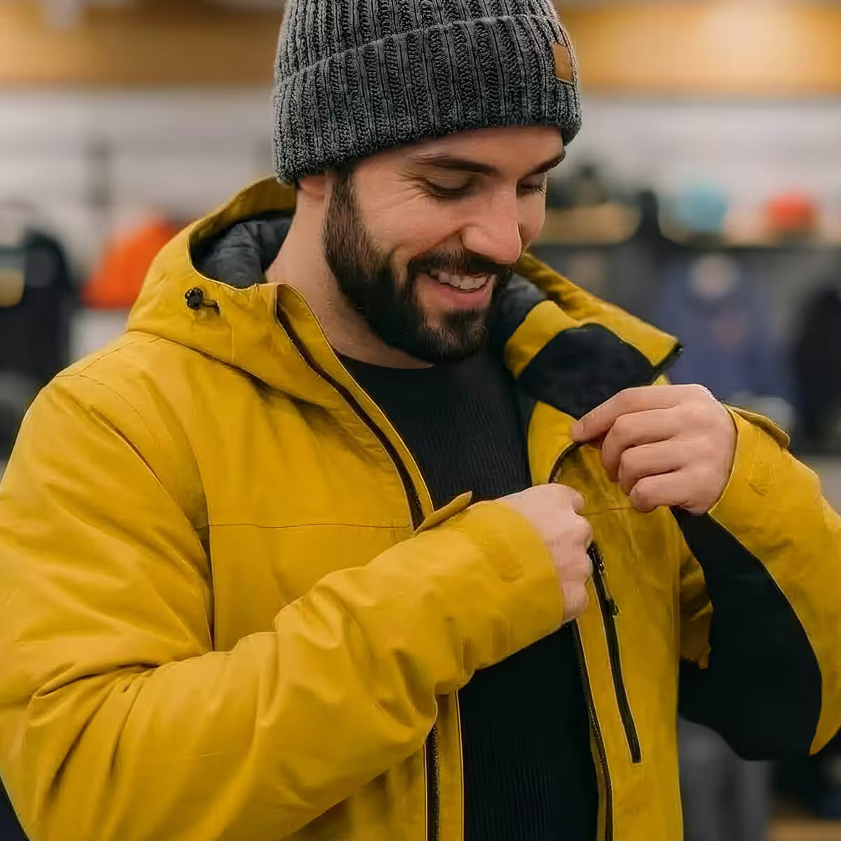 Man wearing a yellow jacket and gray beanie adjusting his jacket in an indoor setting.