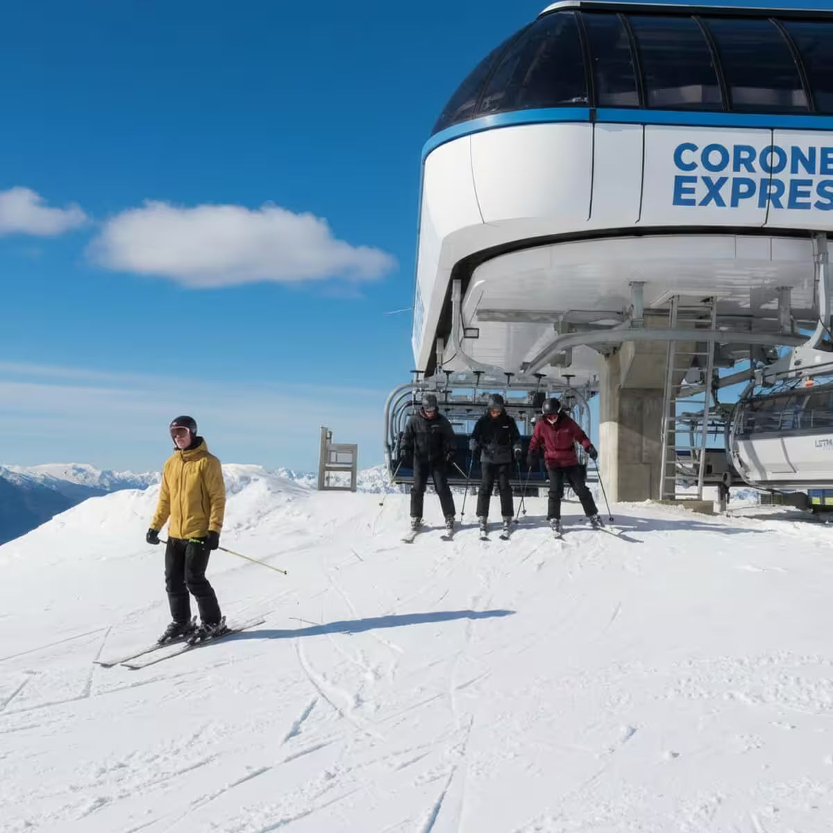 Group of skiers in front of a ski lift named 'Corone Express' on a snowy mountain.