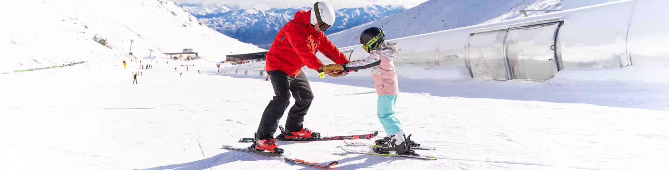 Two people on skis in a snowy landscape with mountains in the background