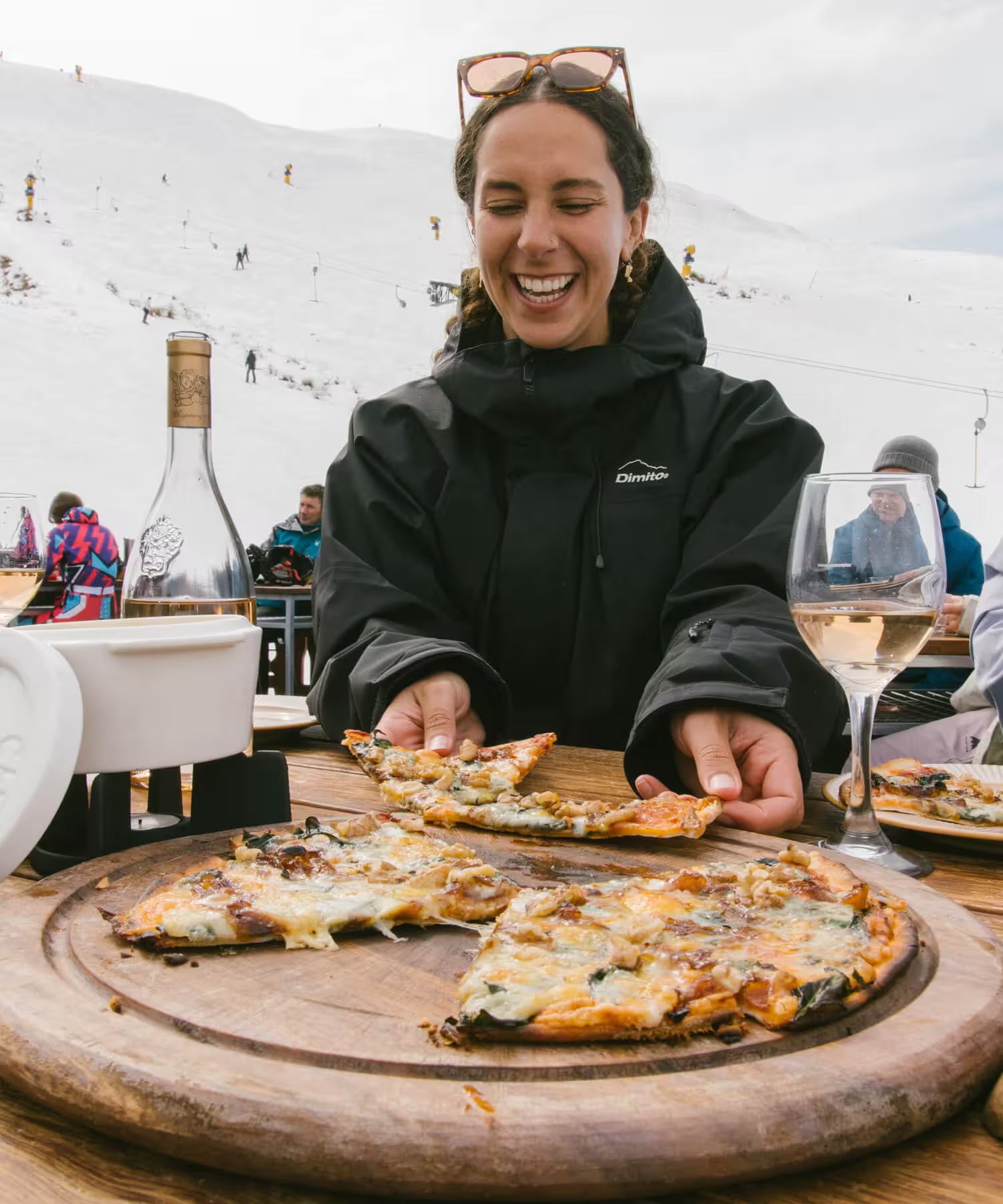 Person in a black jacket serving pizza on a wooden board with a snowy landscape in the background