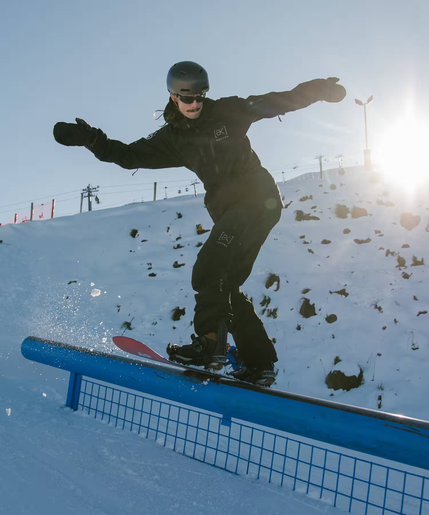 Person snowboarding on a rail with a snowy landscape and clear sky