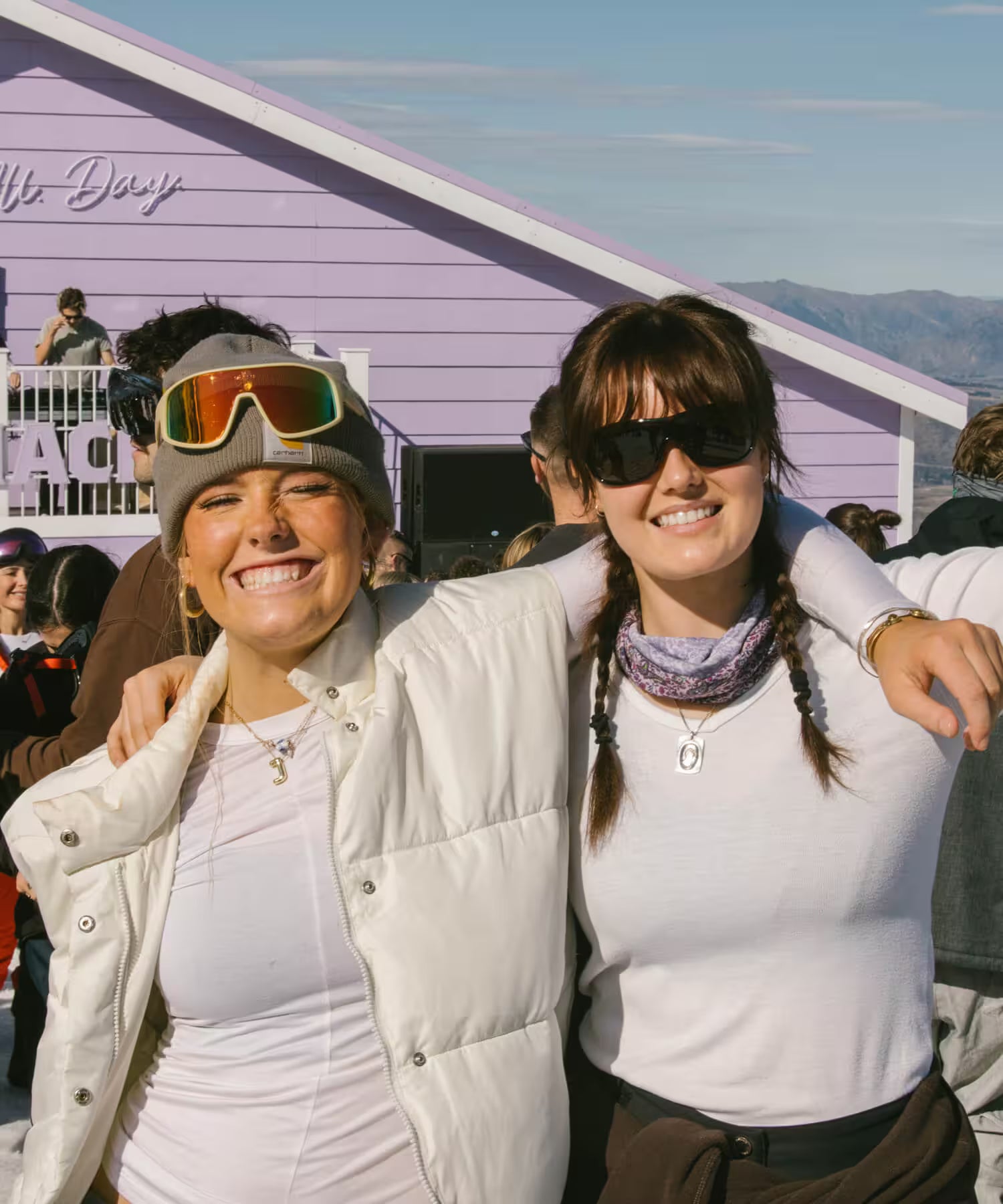 Two women posing together in front of a purple building with mountains in the background