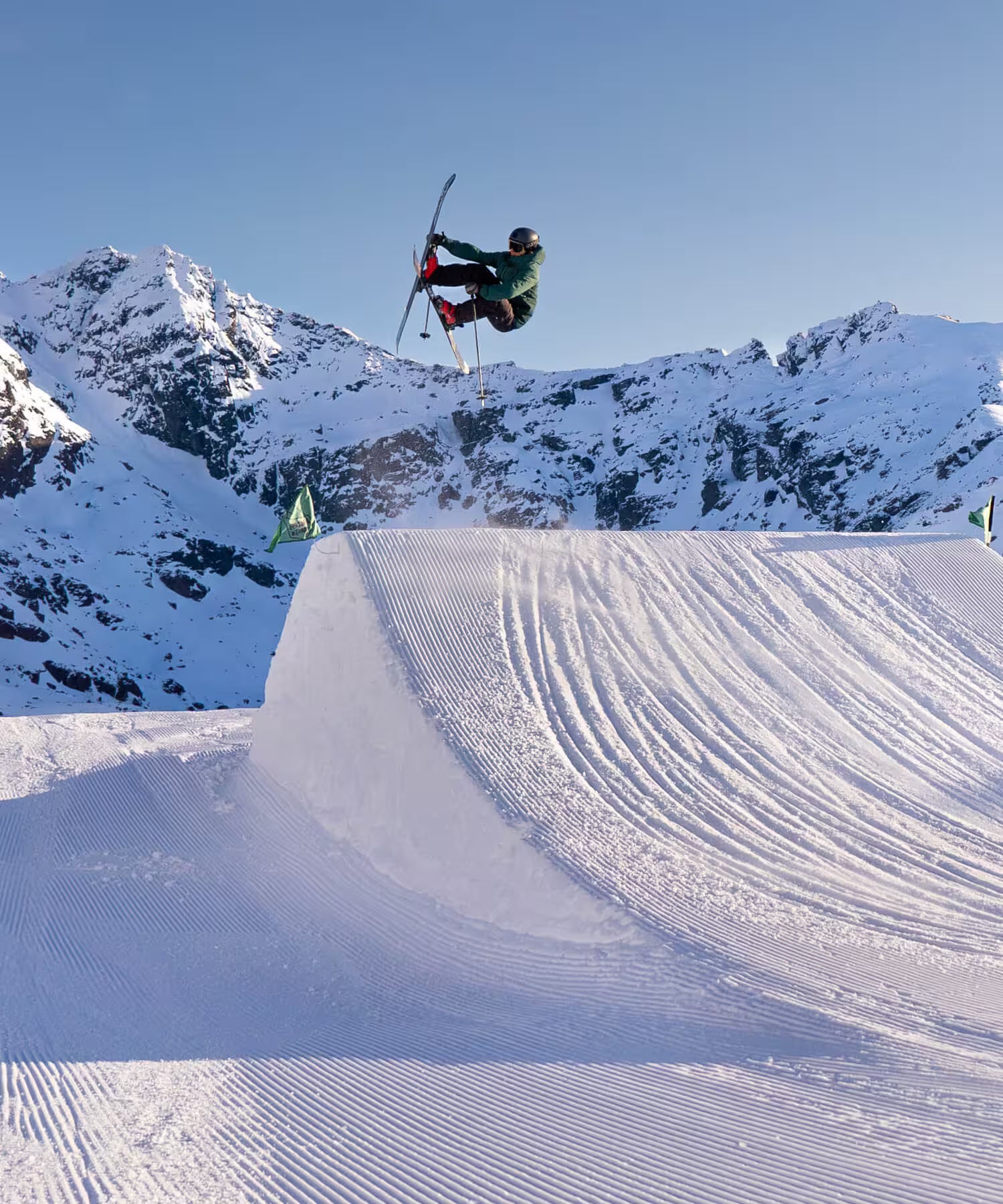 Person skiing off a ramp with snow-covered mountains in the background