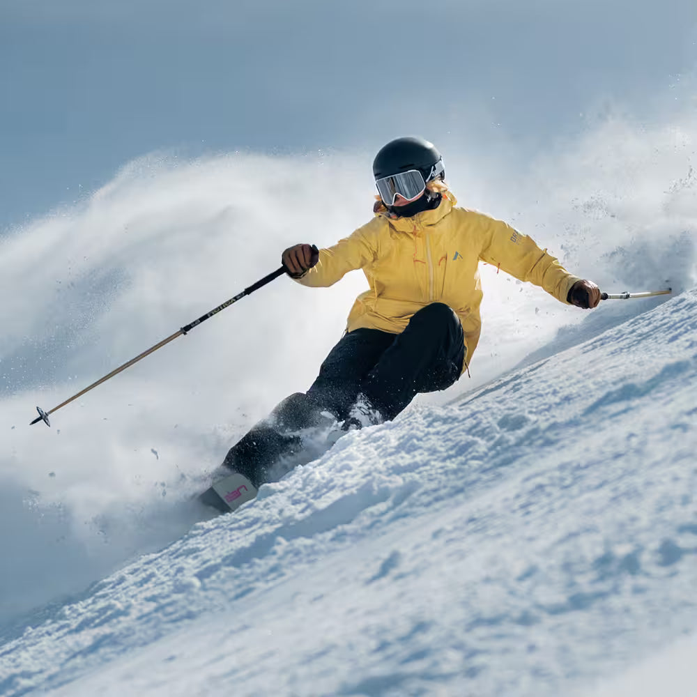 Person skiing down a snowy slope with a yellow jacket and helmet.