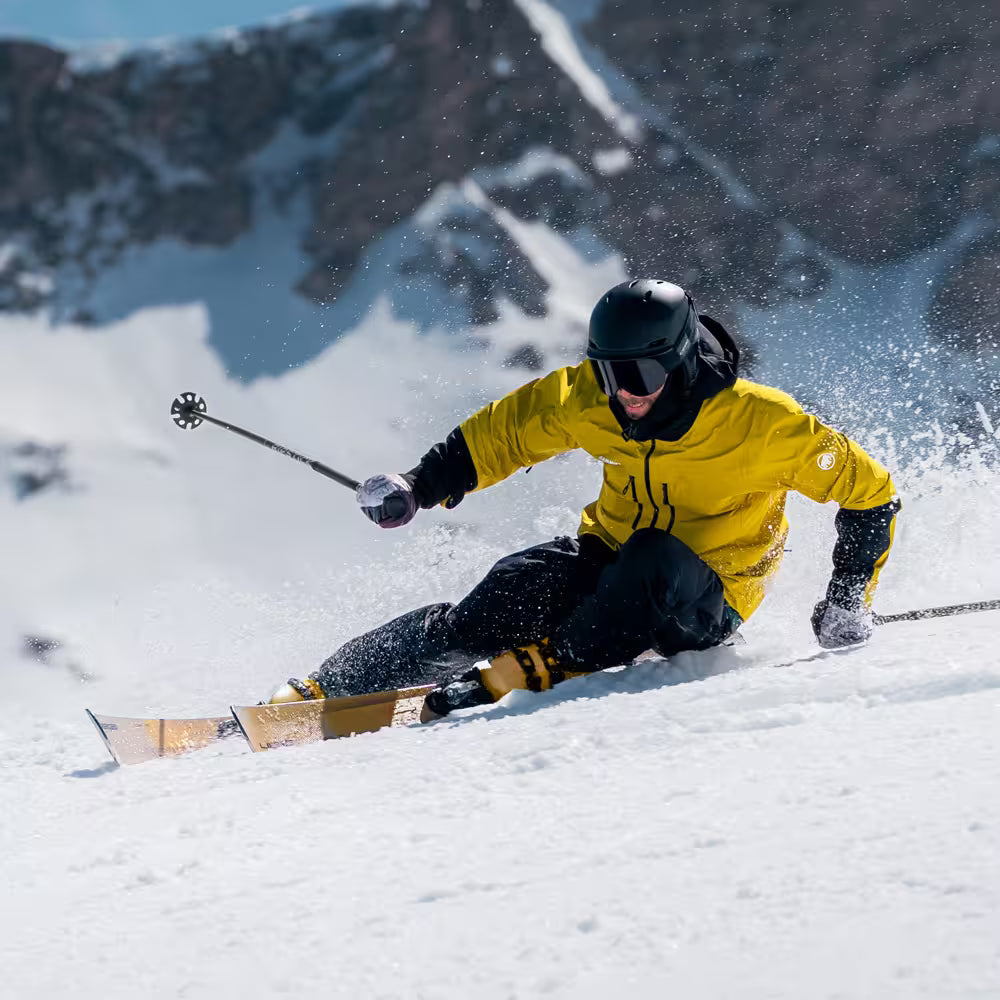 Skier in a yellow jacket carving through snow with mountains in the background