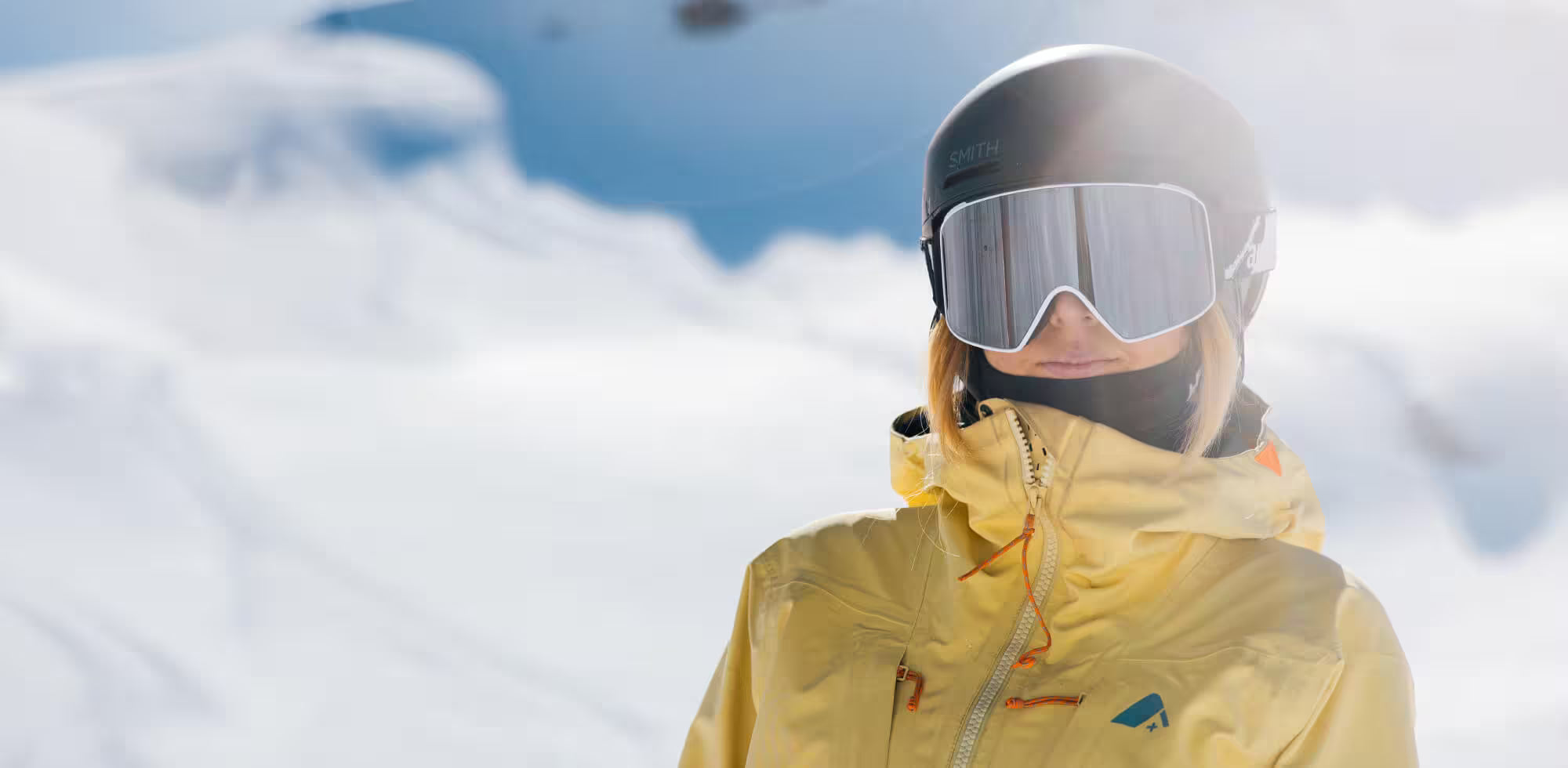 Person wearing a yellow jacket and helmet with goggles in a snowy landscape