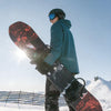 Person holding a snowboard with a red and black design against a snowy background